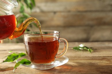 Photo of Pouring freshly brewed tea from teapot into glass cup on wooden table, closeup