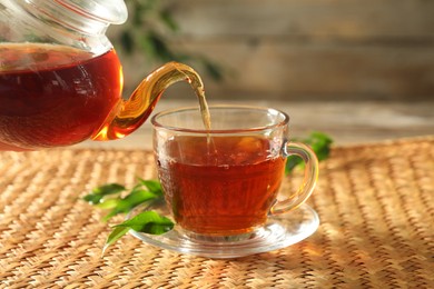 Photo of Pouring freshly brewed tea from teapot into glass cup on wooden table, closeup