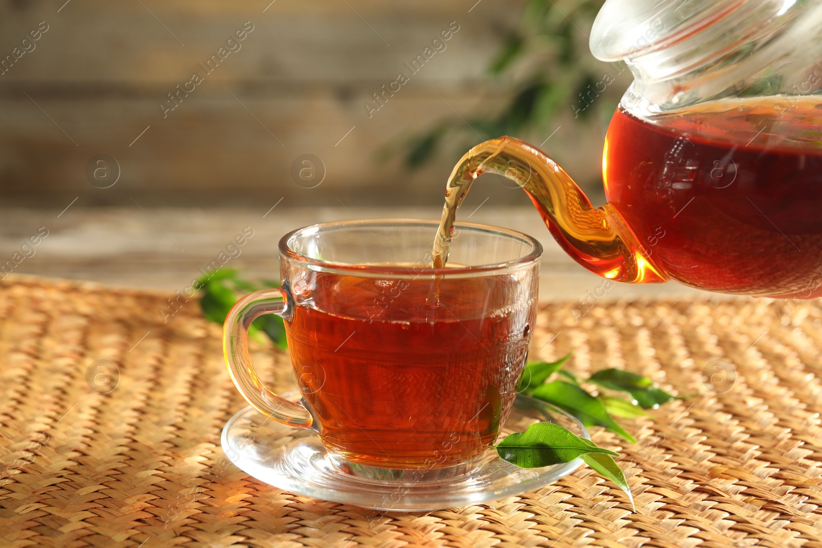 Pouring freshly brewed tea from teapot into glass cup on wooden table, closeup Photo of Pouring freshly brewed tea from teapot into glass cup on wooden table, closeup