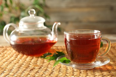 Photo of Freshly brewed tea in glass cup and teapot on wooden table