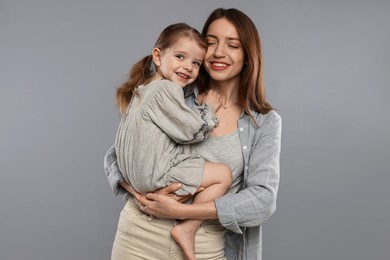 Happy mother with her cute little daughter on grey background