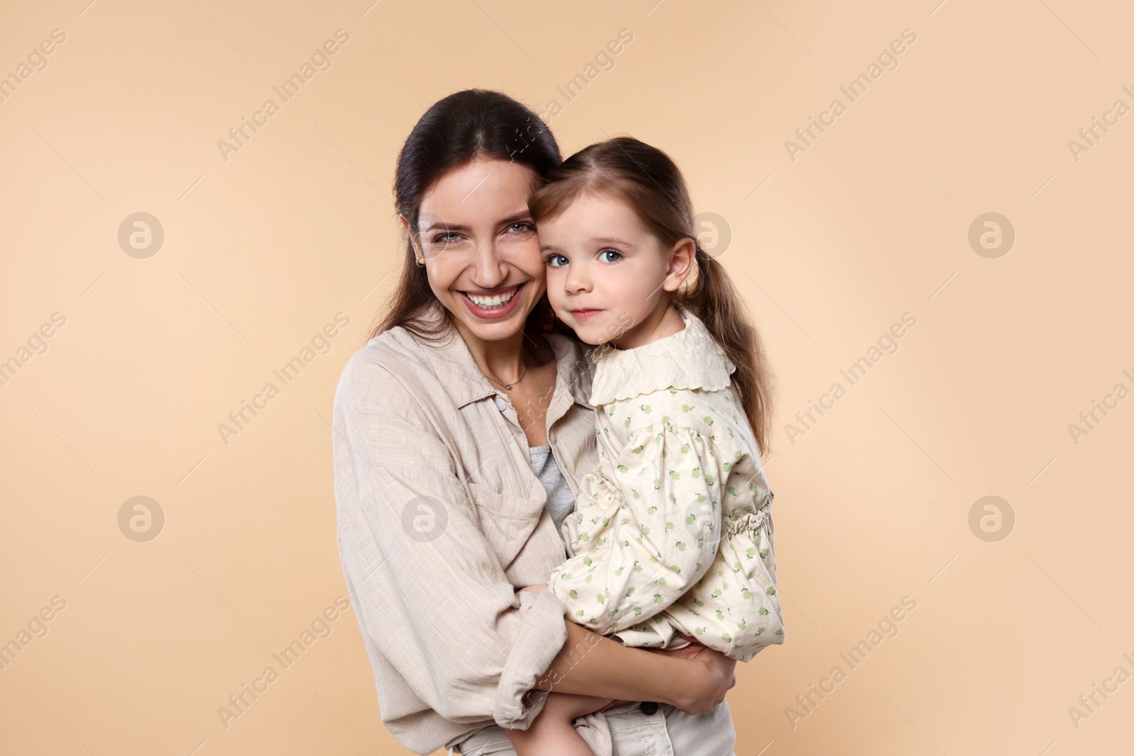 Photo of Portrait of happy mother with her cute little daughter on beige background