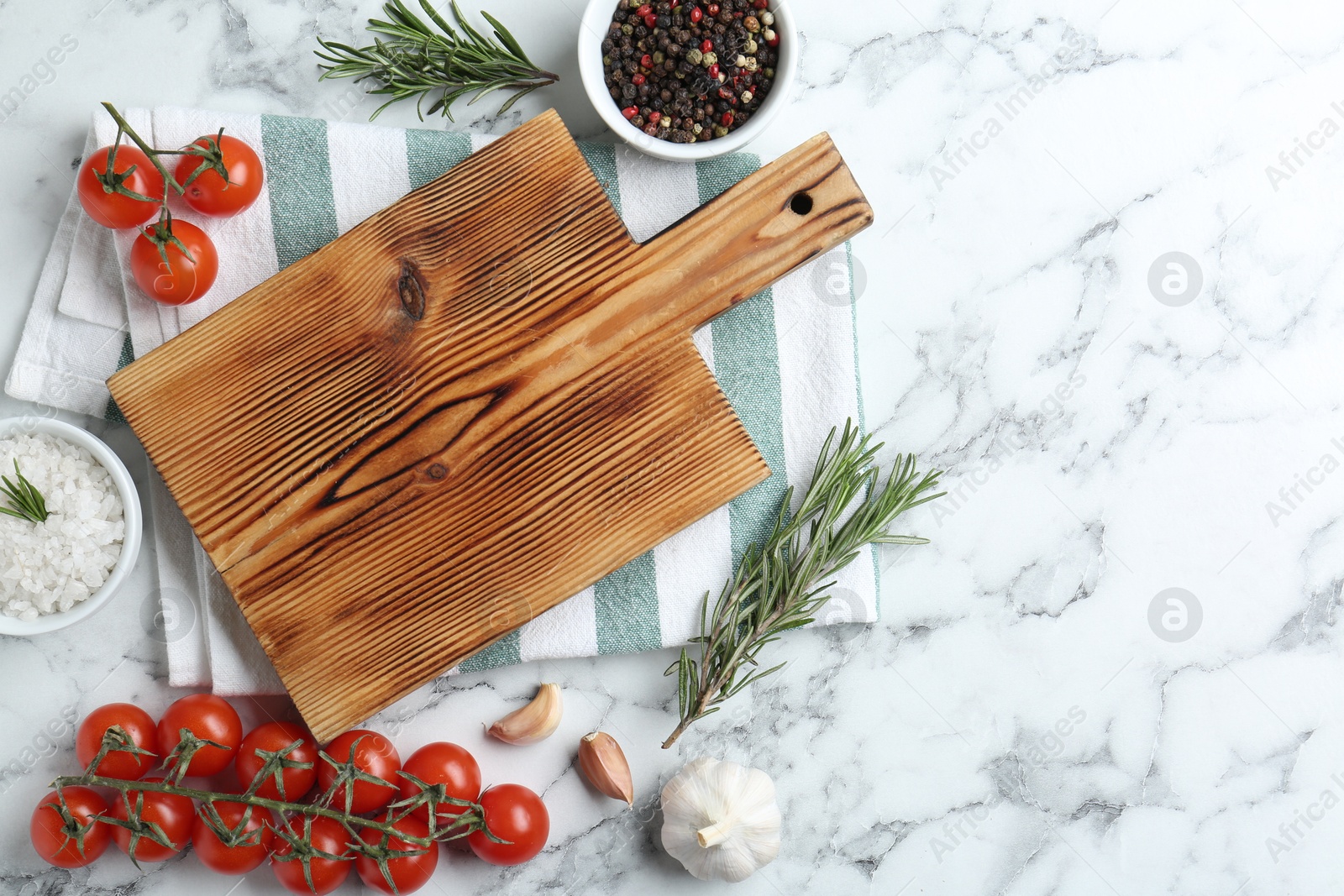 Photo of Wooden cutting board and different products on white marble, flat lay. Space for text