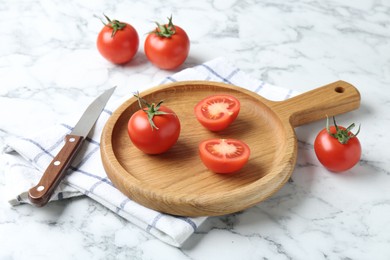 Photo of Wooden cutting board, tomatoes and knife on white marble table