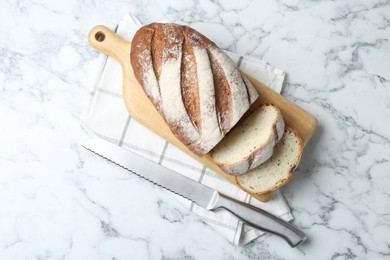 Photo of Wooden cutting board, loaf of bread and knife on white marble table, top view