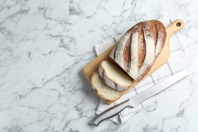 Photo of Wooden cutting board, loaf of bread and knife on white marble table, top view. Space for text