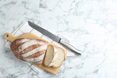 Photo of Wooden cutting board, loaf of bread and knife on white marble table, top view. Space for text