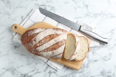 Photo of Wooden cutting board, loaf of bread and knife on white marble table, top view