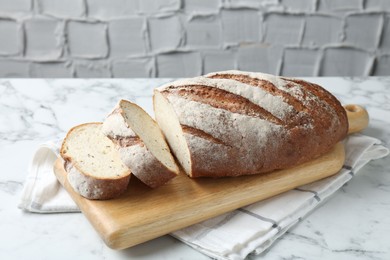 Photo of Wooden cutting board and loaf of bread on white marble table