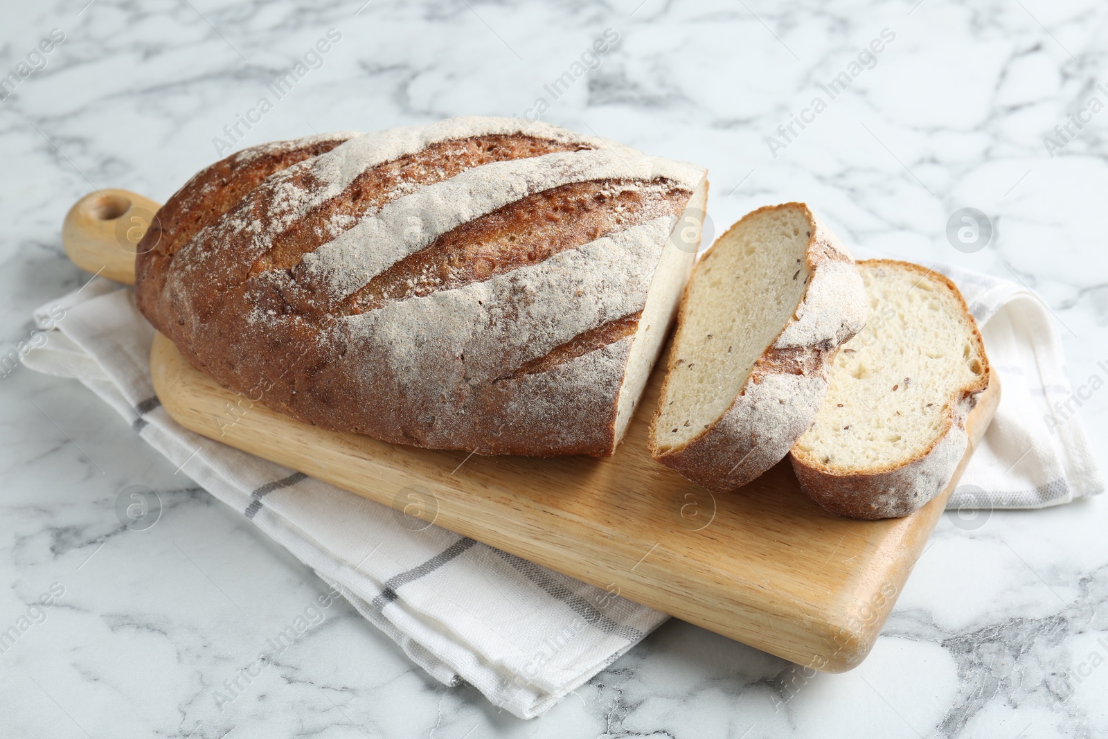 Photo of Wooden cutting board and loaf of bread on white marble table