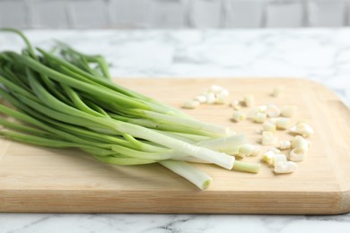 Photo of Wooden cutting board and green onions on white marble table, closeup