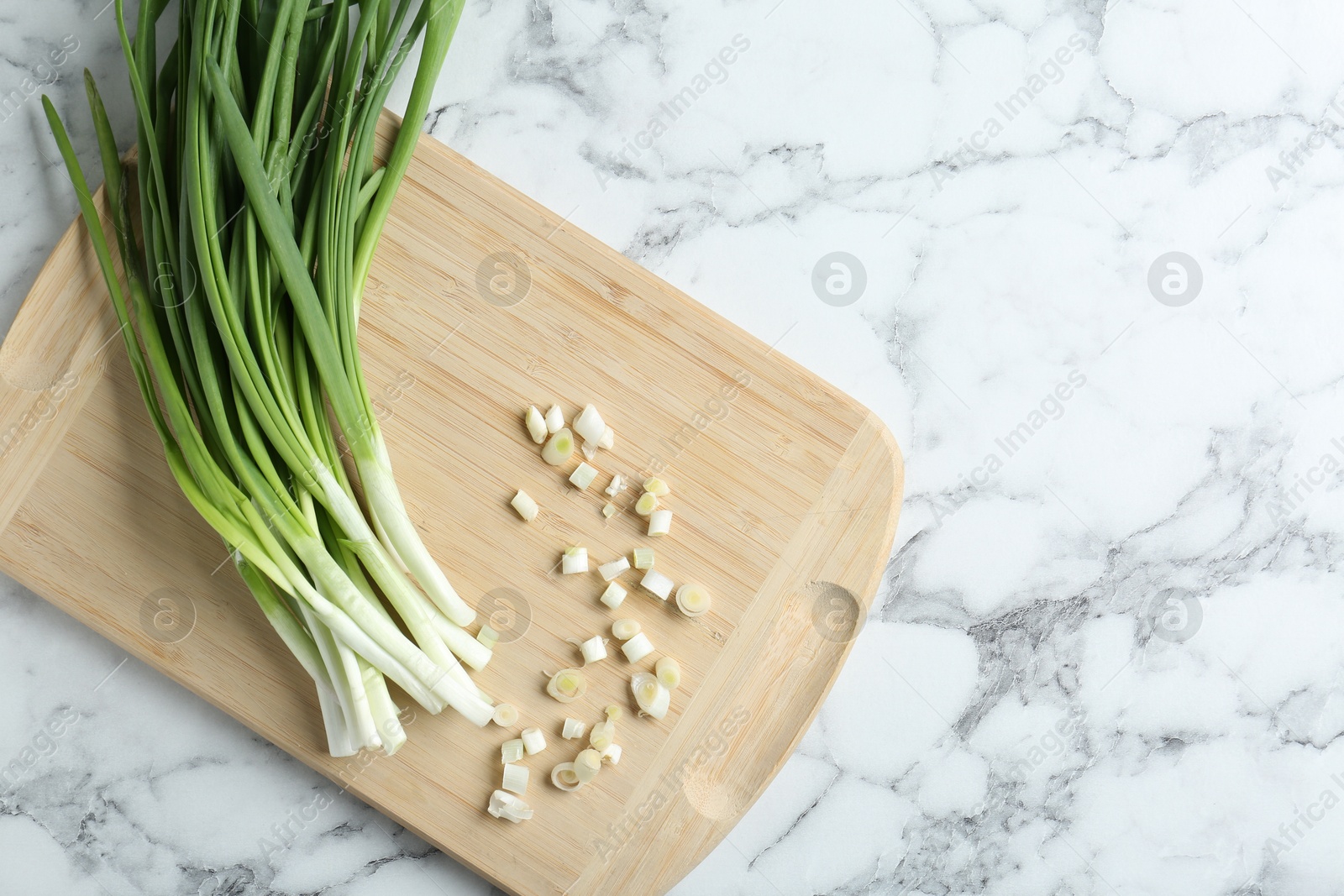 Photo of Wooden cutting board and green onions on white marble table, top view. Space for text