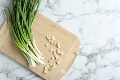 Photo of Wooden cutting board and green onions on white marble table, top view. Space for text