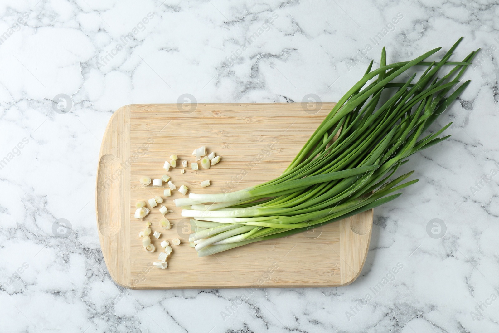 Photo of Wooden cutting board and green onions on white marble table, top view