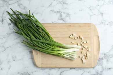 Photo of Wooden cutting board and green onions on white marble table, top view