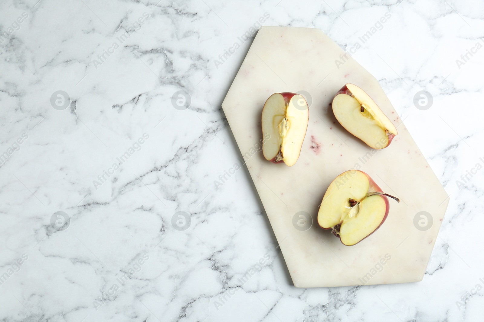 Photo of Cutting board and cut apples on white marble table, top view. Space for text