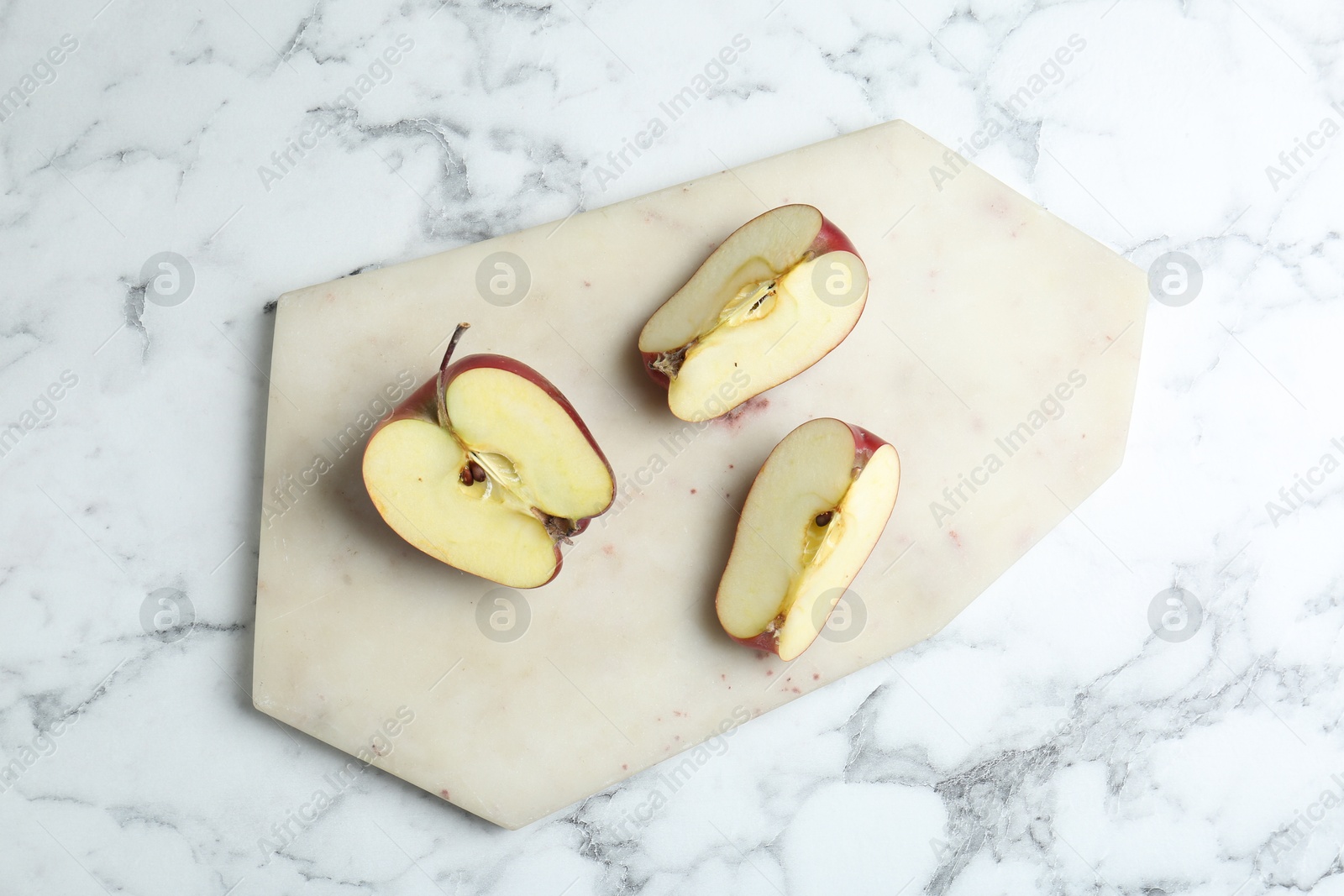 Photo of Cutting board and cut apples on white marble table, top view