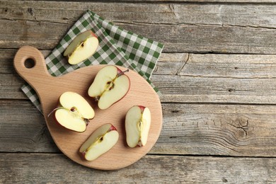 Photo of Cutting board and cut apples on wooden table, top view. Space for text