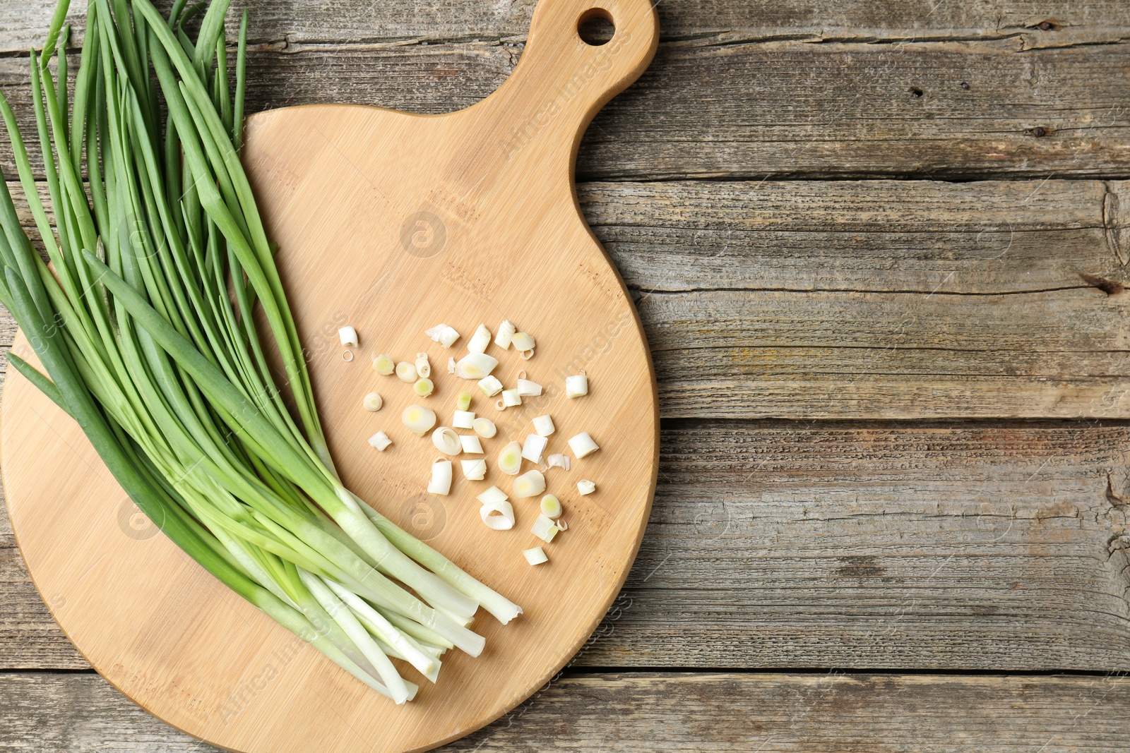 Photo of Cutting board and green onions on wooden table, top view. Space for text