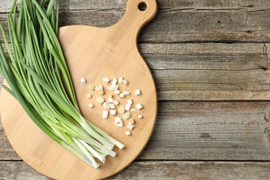 Photo of Cutting board and green onions on wooden table, top view. Space for text