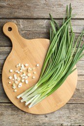 Photo of Cutting board and green onions on wooden table, top view