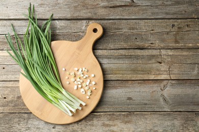 Photo of Cutting board and green onions on wooden table, top view. Space for text