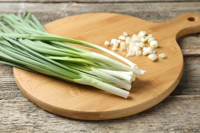 Photo of Cutting board and green onions on wooden table, closeup