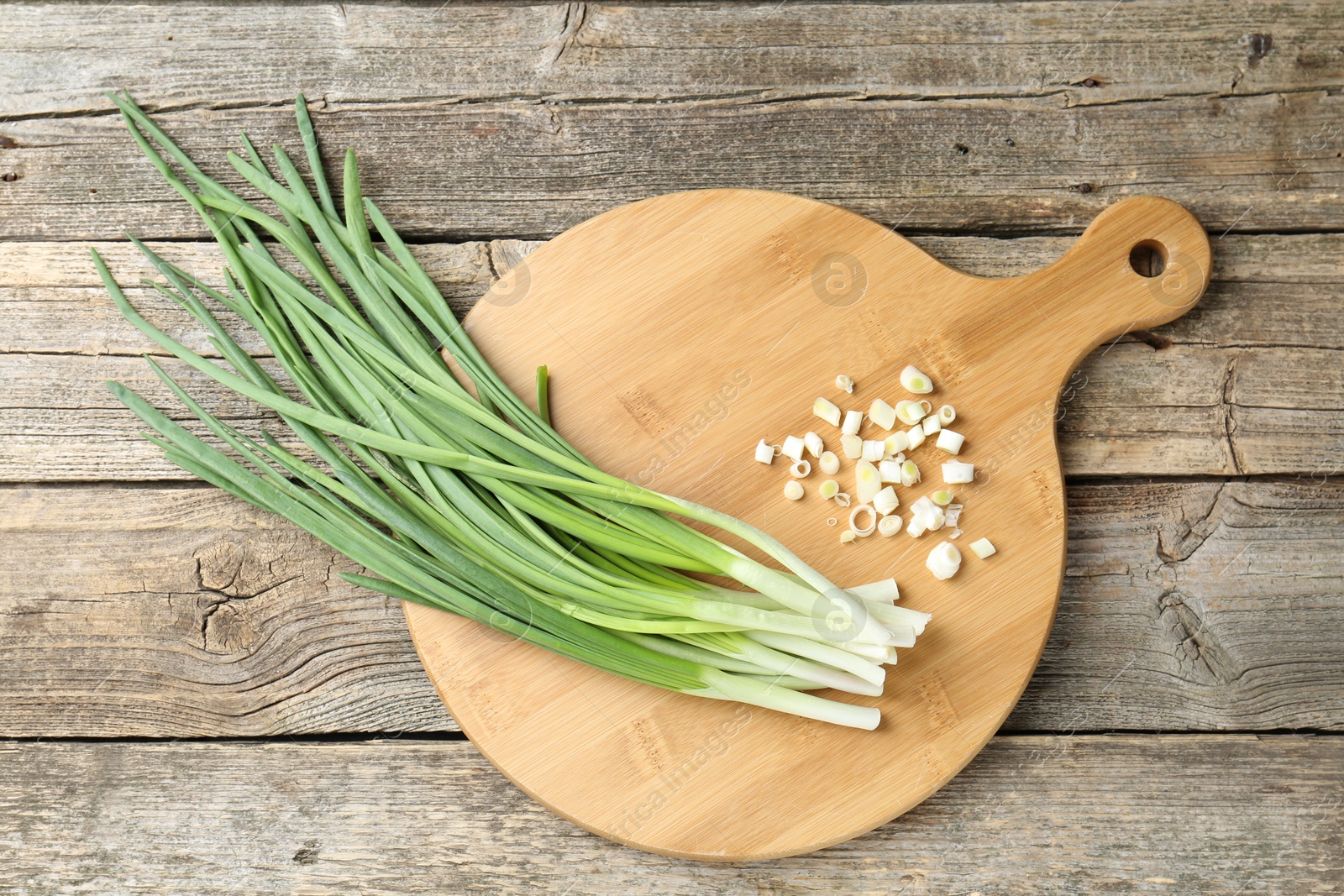 Photo of Cutting board and green onions on wooden table, top view