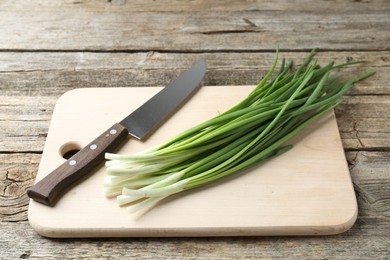 Photo of Cutting board, green onions and knife on wooden table