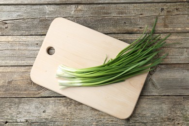 Photo of Cutting board and green onions on wooden table, top view