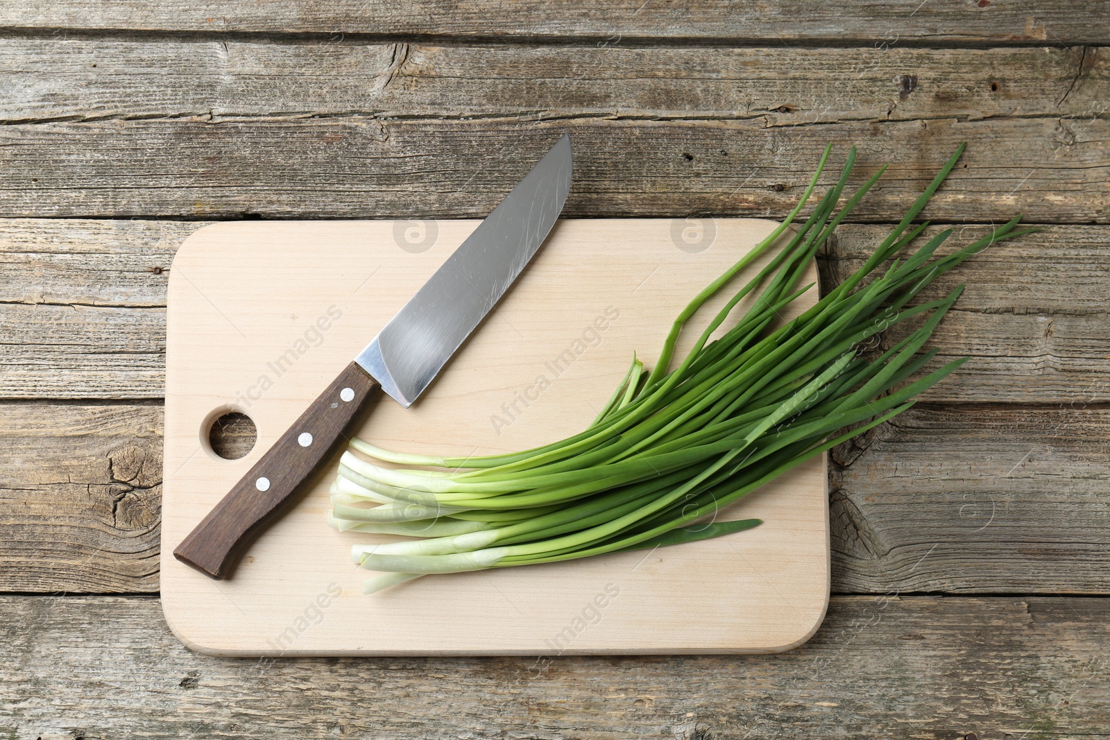 Photo of Cutting board, green onions and knife on wooden table, top view