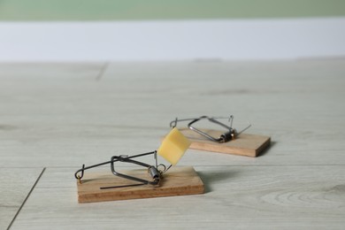 Photo of Spring-loaded bar mousetraps with piece of cheese indoors, selective focus