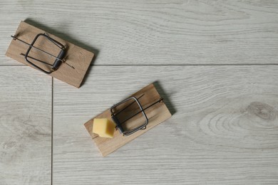 Photo of Spring-loaded bar mousetraps with piece of cheese on floor, flat lay. Space for text