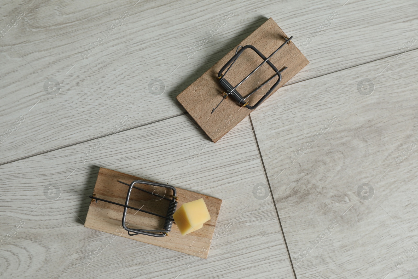 Photo of Spring-loaded bar mousetraps with piece of cheese on floor, flat lay