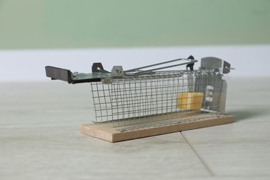 Photo of Metal mouse trap with piece of cheese indoors