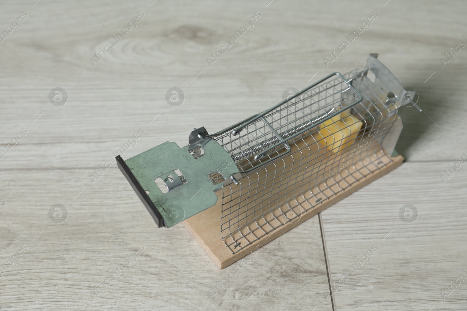 Photo of Metal mouse trap with piece of cheese indoors, closeup