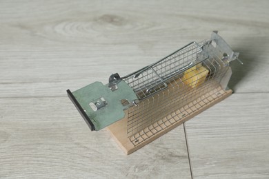 Photo of Metal mouse trap with piece of cheese indoors, closeup