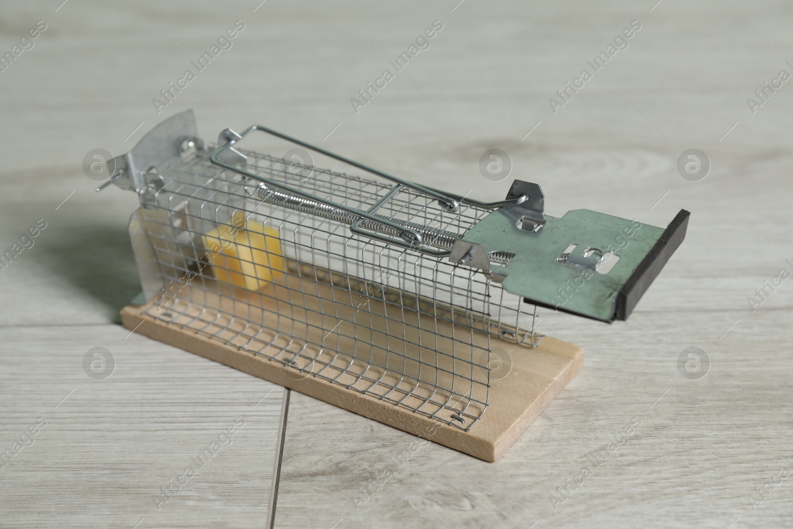 Photo of Metal mouse trap with piece of cheese indoors, closeup