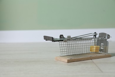 Photo of Metal mouse trap with piece of cheese indoors, space for text