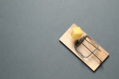 Photo of Spring-loaded bar mousetrap with piece of cheese on gray background, top view. Space for text