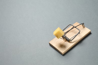 Photo of Spring-loaded bar mousetrap with piece of cheese on gray background, space for text