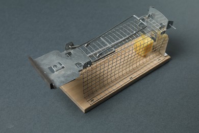 Photo of Metal mouse trap with piece of cheese on gray background, closeup