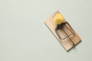 Photo of Spring-loaded bar mousetrap with piece of cheese on light background, top view. Space for text