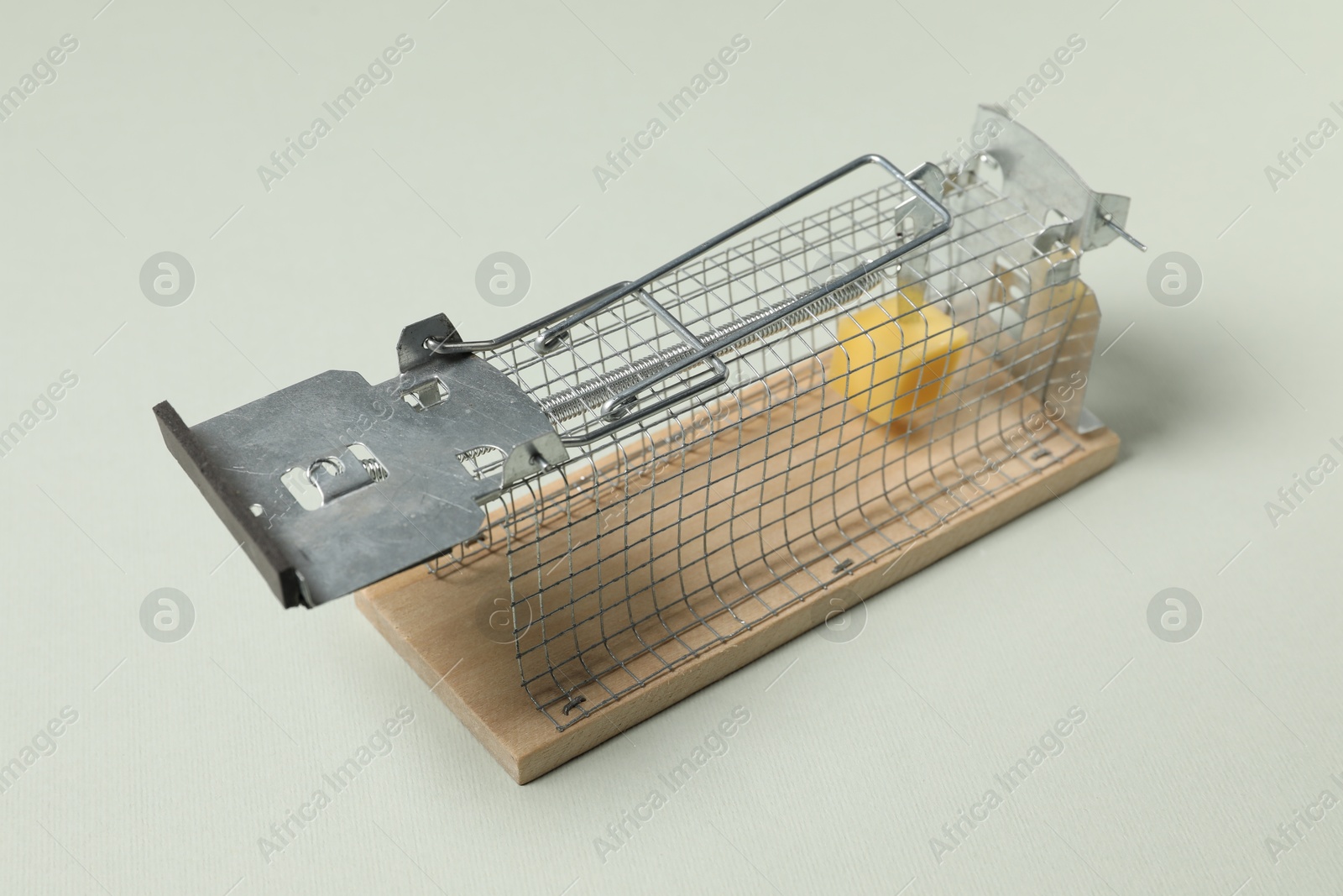 Photo of Metal mouse trap with piece of cheese on light background, closeup