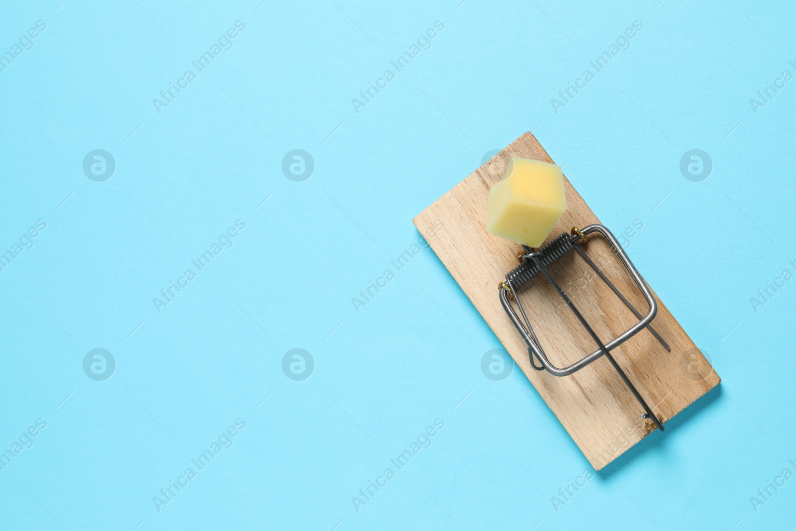 Photo of Spring-loaded bar mousetrap with piece of cheese on light blue background, top view. Space for text