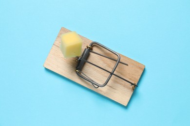 Photo of Spring-loaded bar mousetrap with piece of cheese on light blue background, top view