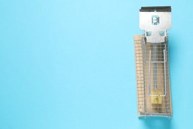 Photo of Metal mouse trap with piece of cheese on light blue background, top view. Space for text