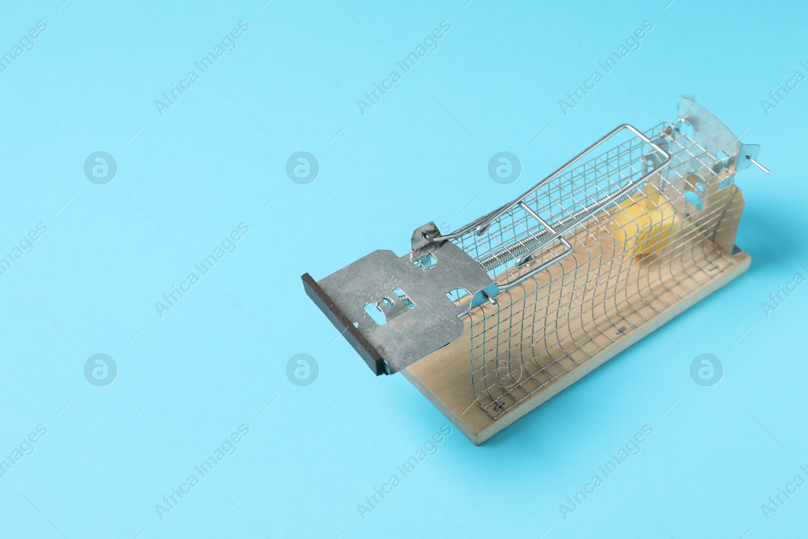 Photo of Metal mouse trap with piece of cheese on light blue background, space for text