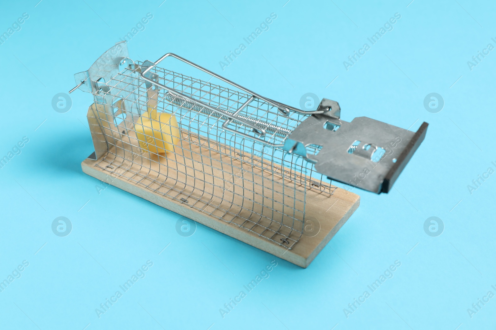 Photo of Metal mouse trap with piece of cheese on light blue background, closeup