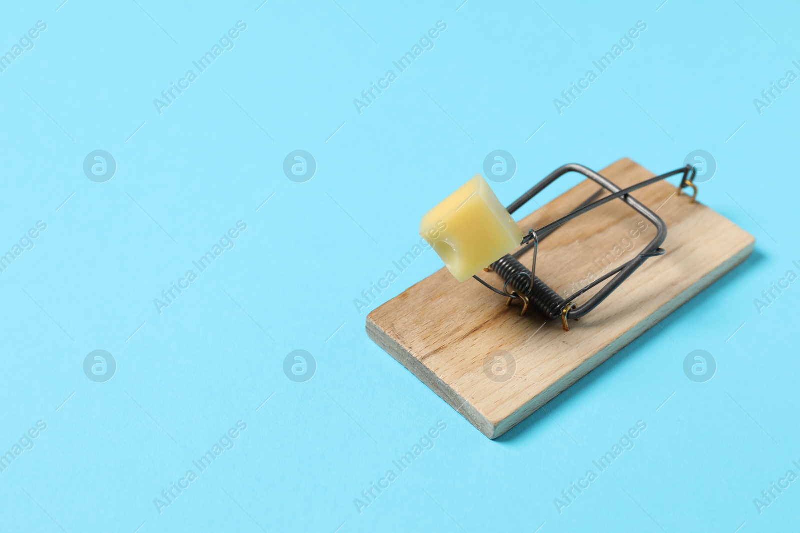 Photo of Spring-loaded bar mousetrap with piece of cheese on light blue background, space for text